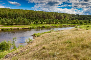 Fototapeta na wymiar River in summer against forest on hills, blue sky and white clouds