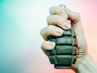 A closeup photo of a hand squeezes a green military grenade on a multicolor background.