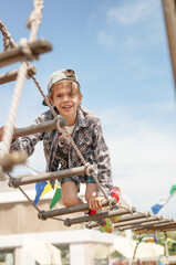 Smiling boy climbing at a playground, focus on rope, stairs