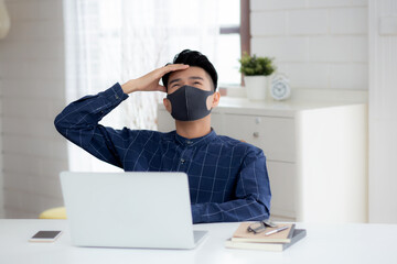 Young business man in face mask working from home with laptop computer and bored on desk for protection for outbreak of covid-19, male quarantine stay home using notebook with unhappy, new normal.