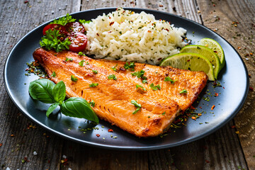 Fried salmon steak with rice and vegetables on wooden table

