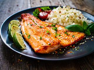 Fried salmon steak with rice and vegetables on wooden table
