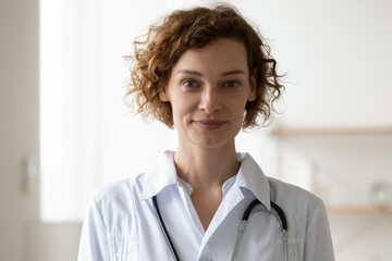 Profile picture of young Caucasian woman doctor or GP in white medical uniform look at camera in...