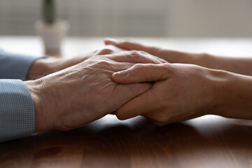 Crop close up of young woman doctor hold elderly male patient hands talk support at consultation in hospital or clinic, caring female nurse or caregiver comfort caress mature man client at meeting