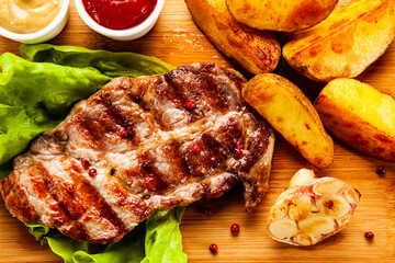 Grilled steak with baked potatoes and vegetables served on wooden board on white background