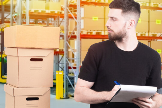 The man makes notes about receiving the goods in the warehouse. A male warehouse worker with a Notebook. Storekeeper next to cardboard boxes. The man in the warehouse.