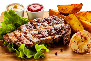 Grilled steak with baked potatoes and vegetables served on wooden board on white background