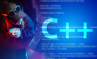 C++ programming language. Large C++ lettering and a girl in a baseball cap at a laptop. Development...