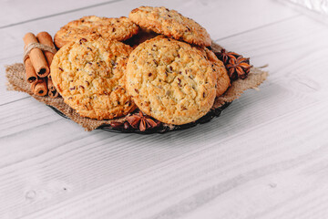  baked oatmeal cookie on plate with napkin decorated with cinnamon sticks, coffee and star anise on white wooden table background. Image use for commercial or menu layout design. Copy space.