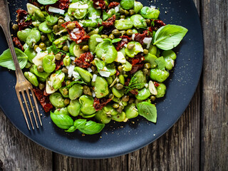 Broad beans salad with sun dried tomatoes, garlic and onion on wooden table
