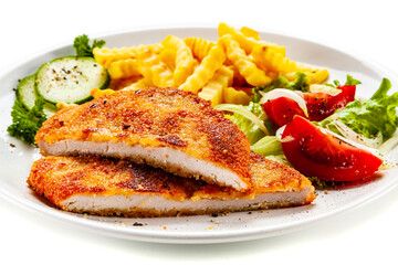 Breaded fried pork chop, French fries and vegetables on white background
