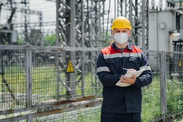 An electrical substation engineer inspects modern high-voltage equipment in a mask at the time of pondemia. Energy. Industry