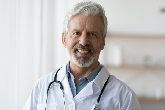 Profile picture of smiling old male doctor in white medical uniform look at camera in hospital private clinic, headshot portrait of happy senior man GP physician show confidence, healthcare concept
