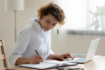 Fototapeta na wymiar Young Caucasian female doctor in white medical uniform sit at desk work on laptop make note in register, woman nurse or GP fill patient anamnesis in journal, use computer in private clinic