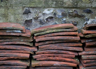 Stacks of old terracotta roof tiles piled against weathered flint wall