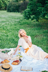 Young beautiful european blonde longhaired girl in white dress at nature.Spends the weekend outside the city, outdoors, a picnic in the park, relaxation, read book.Summer time
Hold bascet with flowers