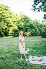 Young beautiful european blonde longhaired girl in white dress at nature.Spends the weekend outside the city, outdoors, a picnic in the park, relaxation, read book.Summer time
Hold bascet with flowers