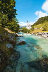 Fototapeta na wymiar Iconic scene of traditional church in bavarian village in the alps with turquiose river