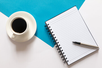Flay lay of coffee, blank notebook and pen on split color blue and white background