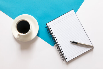 Flat lay of coffee, notebook and pen on split color blue and white background