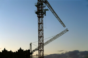 Cranes are silhouetted at a construction site at sunset