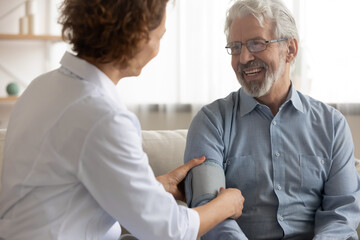 Attentive female nurse measure low high blood pressure of smiling mature male patient at home visit...