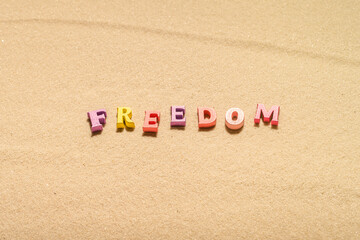 Colorful freedom word made from  letters on the sand beach. Travel relaxation concept. Creative