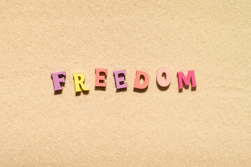 Colorful freedom word made from  letters on the sand beach. Travel relaxation concept. Creative