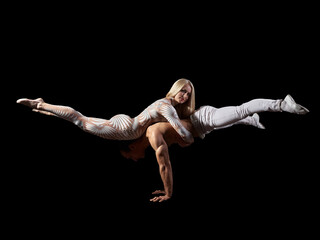 Couple acrobats perform a trick handstand, body balance, isolated on a black background. A girl in a white suit, a guy with a naked muscular torso and white pants. © Tigran Gasparyan