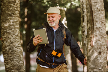 Adult male hiker using digital tab and looking for location during hike in nature.