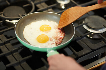Above view close up of unrecognizable woman cooking breakfast in home kitchen with focus on frying eggs in pan, copy space