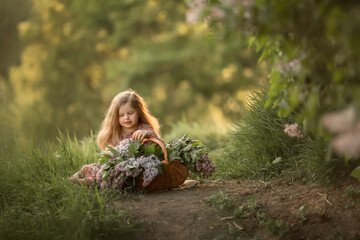 A little girl is standing near a large lilac Bush and playing with a basket filled with flowers. Image with selective focus and noise effect.