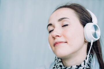 Caucasian girl in headphones smiles and listens to music with her eyes closed.