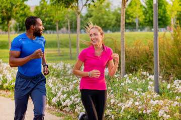 Young couple is jogging in the park out to run together. Afro american man and beautiful blonde girl in sportswear running through the city park together. Health and fitness