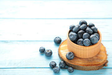 Fresh blueberries in small wooden bowl on blue background