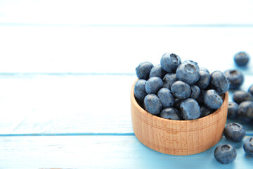 Fresh blueberries in small wooden bowl on blue background