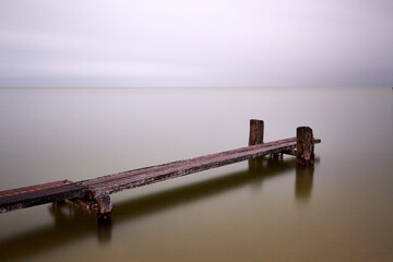 Lonely wooden foot jetty points out to silky smooth water slowed down with long exposure giving...