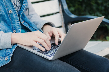 Caucasian man sitting on a bench and typing on a laptop