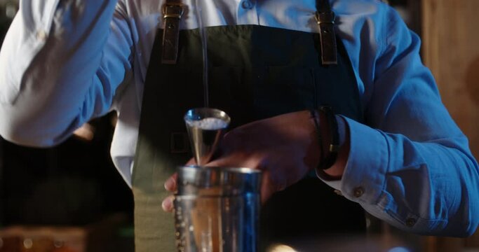 Professional bartender masterly creating a cocktail in modern bar. Experienced barman adding syrip into shaker using jigger - food and drink, nightlife close up 4k footage