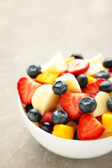 Fresh fruit salad in bowl on grey concrete background. Vertical foto