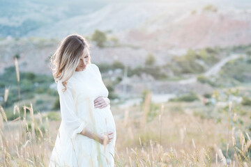 Fototapeta na wymiar Beautiful pregnant woman 25-30 year old wearing white dress posing in meadow outdoors close up. Motherhood. Maternity. 20s.