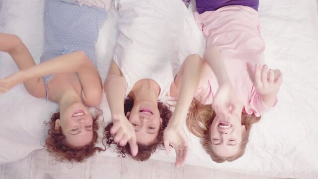 Top view. Happy girl stay at home lying on bed and looking at the ceiling. Three young girls smiling telling a jokes. Free time concept. Friends concept. Prores 422. 