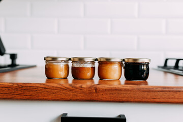 Little honey cans on the wooden table. Honey variety cans in a row. Bright kitchen interior. Wooden complete kitchen with gas oven