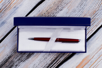Topview red pen in a blue gift box. Expensive luxury pen as a present. White rustic wooden background.