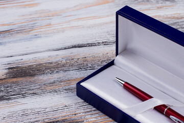 Closeup metal red pen in a gift box. White wooden background.