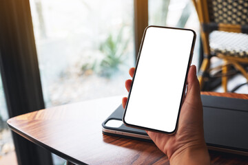 Mockup image of a hand holding mobile phone with blank white screen in cafe