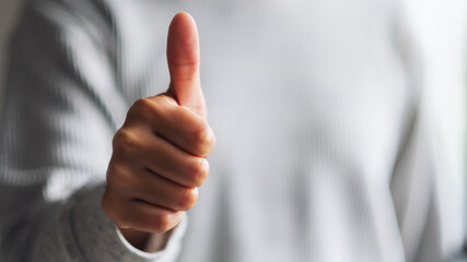 Closeup image of a woman making and showing thumbs up hand sign