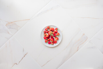 Obraz na płótnie Canvas A plate of strawberries on white marble tile with copy space. Red berries on a white kitchen, summer concept