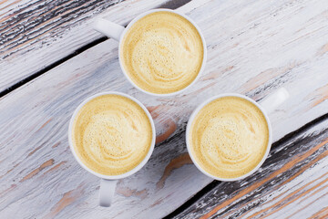 Topview three cups of foamy coffee or cappuccino. White wooden background.