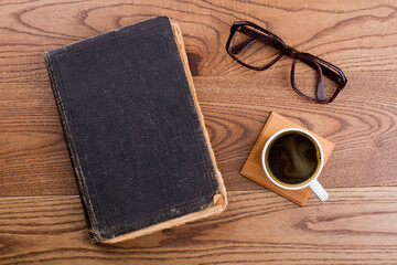 Old book with cup of coffee and glasses. Topview flat lay. Brown wooden background.